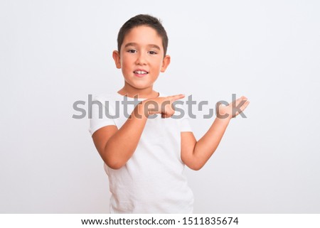 Beautiful kid boy wearing casual t-shirt standing over isolated white background amazed and smiling to the camera while presenting with hand and pointing with finger.