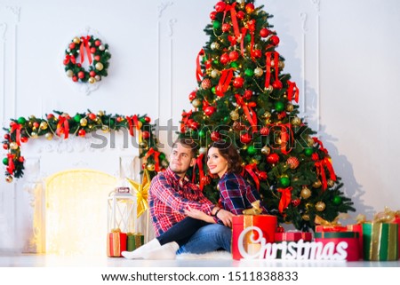 a couple in love sitting at the fireplace and christmas tree and the gifts around them and they look into the distance