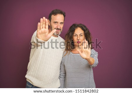 Beautiful middle age couple wearing winter sweater over isolated purple background doing stop sing with palm of the hand. Warning expression with negative and serious gesture on the face.