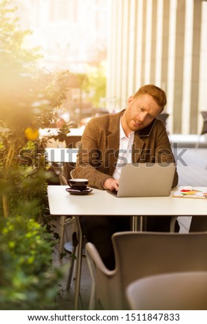 Hardworking elegant man texting from his laptop and having conversation via mobile phone