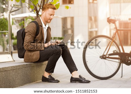 Concentrated stylish man sitting on border and using a laptop while working on new project