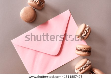 Pink envelope and dark chocolate macarons on bronze background.