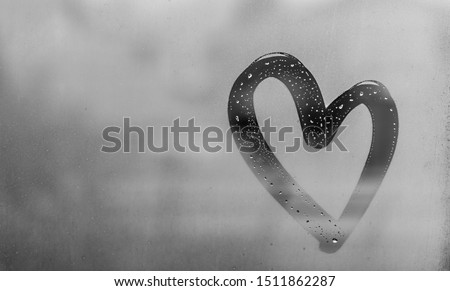 Heart painted on sweaty glass, there are many drops on it, inscription heart and love using handmade on a wet gray autumn foggy glass. valentines day concept with copy space for text
