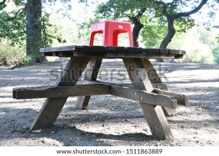 Small red plastic stool on top of pick-nick bench, abstract play objects within nature with forest in the background.
Land Art Photography.