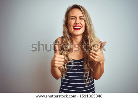 Young beautiful woman wearing stripes t-shirt standing over white isolated background success sign doing positive gesture with hand, thumbs up smiling and happy. Cheerful expression and winner gesture