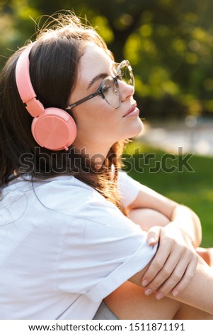 Photo of a serious student lady outdoors in nature green park listening music with headphones.