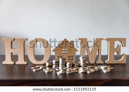Home model and alphabet word home with coins stack on wooden table and white background, money, financial, saving, business concept 