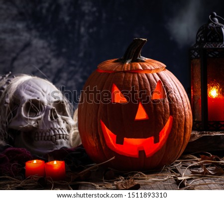 Glowing Jack-O-Lantern with burning candles and skull on a wooden surface and dark background