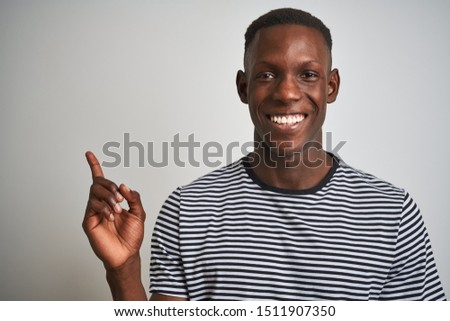 African american man wearing navy striped t-shirt standing over isolated white background very happy pointing with hand and finger to the side