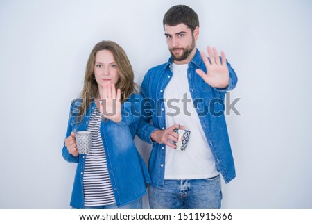 Young beautiful couple drinking a cup of coffee over white isolated background with open hand doing stop sign with serious and confident expression, defense gesture