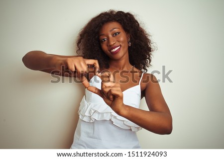 Young african american woman wearing t-shirt standing over isolated white background smiling in love showing heart symbol and shape with hands. Romantic concept.