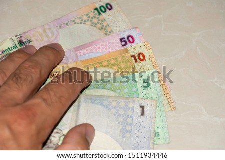 A hand reaches out to fanned out cash bills of Qatar, the currency called the Qatari Riyal notes of cash spread out on the white background. Money exchange.