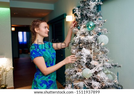 Cute young woman in the dress decorates a Christmas tree with artificial snow in silver tone.