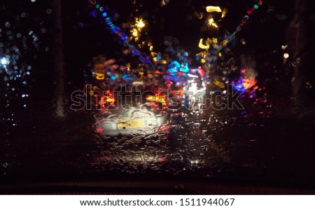 Abstract painterly rain drops on a car window with vibrant city and street lights out of focus in the background. Tired and drunk driving in wet and rainy conditions. safe drive                      