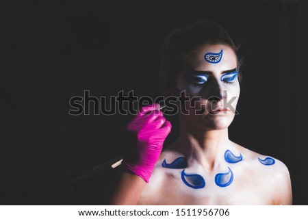 Hand in glove is painting oriental patterns on the skin of a woman, photo isolated on black background. Body art. Body painting. Art concept