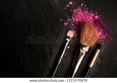 Make-up brushes with crushed cosmetics, shot from the top on a black background with copy space, a beauty design template for a makeup banner