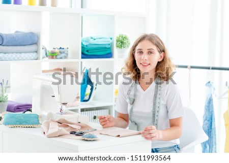 Smiling seamstress sitting at working desk with measuring tape