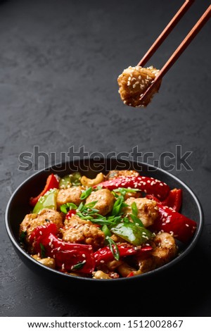 Schezwan Chicken or Dragon Chicken in black bowl at dark slate background. Szechuan Chicken is popular indo-chinese spicy dish with chilli peppers, chicken and vegetables.