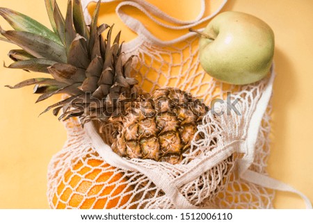 Mesh shopping bag with lemons and pineapple on pastel pink canvas background.