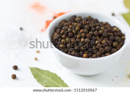 black papper corn in white bowl and colorful spices on a white background