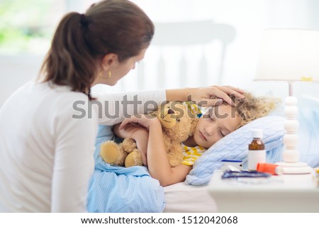 Sick little boy with asthma medicine. Mother with ill child lying in bed. Unwell kid with chamber inhaler for cough treatment. Flu season. Parent in bedroom or hospital room for young patient.  Royalty-Free Stock Photo #1512042068