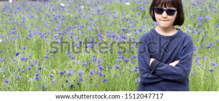 critical child thinking, biting lips with sunglasses and arms crossed for skeptical body language, copy space flower meadow background