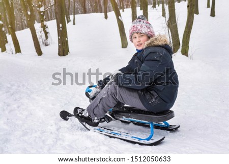  A boy rides a snow scooter outdoors in winter. Winter vacation and holidays.
