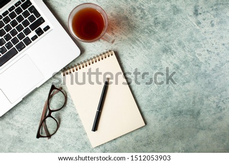 office items laptop, glasses, notebook, mug of tea pen on a light table