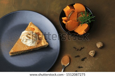 A slice of homemade sweet pumpkin pie and pumpkin pieces on brown background. Top view