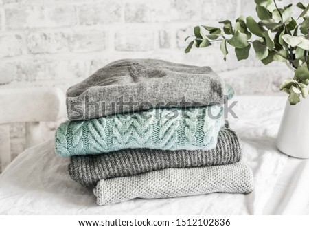 Stack of cozy winter autumn sweaters pullovers on the table on a light background                   