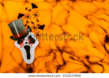 Halloween postcard. Тraditional festival of autumn. Decoration and party concept .Paper mask with bats, spiders on the webon a orange background .Flat lay, top view, copy space
