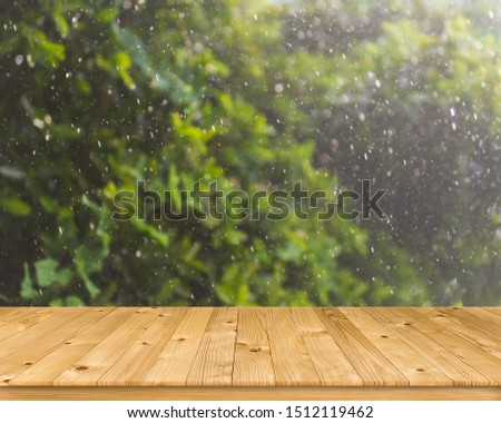 Empty old brown plank wooden board as mock up display shelf with blurred natural picture from fresh green leaves tree with group of fall droplet’s motion and bokeh from hard rainy background. 
