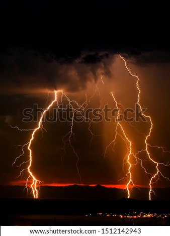 Three-branched lightning strike during desert storm at late twilight so the glow of the sunset highlights the mountains in the background. Room for text or ad.