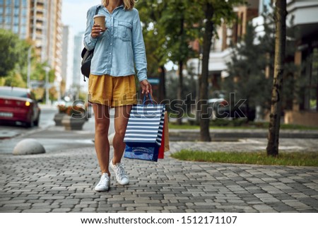 Cropped photo of a woman outdoors with a paper cup of coffee and colorful shopping bags. Website banner