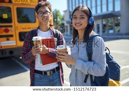 Smiling young girl in headphones near school bus stock photo