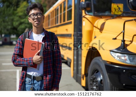 Happy male student standing near school bus stock photo