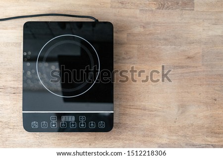 Top view of burner on small electric stove with control panel. Modern kitchen appliance on wooden table with copy space Royalty-Free Stock Photo #1512218306