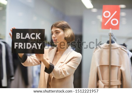 Waist up portrait of beautiful woman hanging Black Friday sale sign on window display in clothes store, copy space
