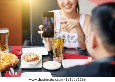 Asian young man on the screen of mobile phone waving to his friends while they have online conversation with him at the restaurant