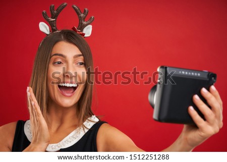 Adult happy woman in Christmas mood taking instant pictures over red background