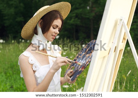 woman in a white hat paints an easel