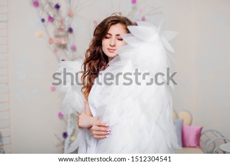 Portrait of a young girl, an angel in a white dress stands wrapped in wings.