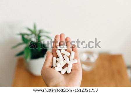 White pills. Dietary supplements.Hand holding magnesium capsules above glass of water on wooden table.  Health support and treatment. Biologically active additives Royalty-Free Stock Photo #1512321758