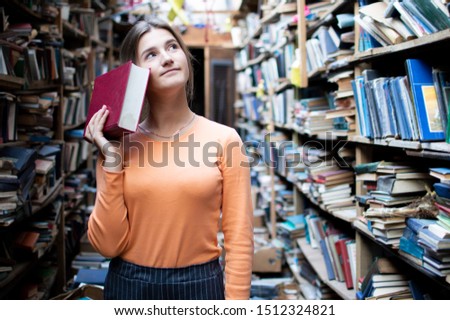 young girl student reads a book in the library, a woman likes to read a lot, she is looking for literature on bookshelves, knowledge is power, concept