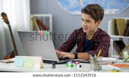 Schoolboy playing online game on laptop at home sitting table, teenage free time Royalty-Free Stock Photo #1512343916
