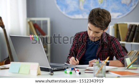 School pupil writing notebook doing home work at table, distance education Royalty-Free Stock Photo #1512343919