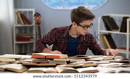 Hardworking male teen searching information sitting table full of books, student Royalty-Free Stock Photo #1512343979