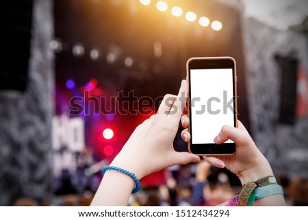 Recording concert by smartphone. Mobile phone in raised hands. Blank screen