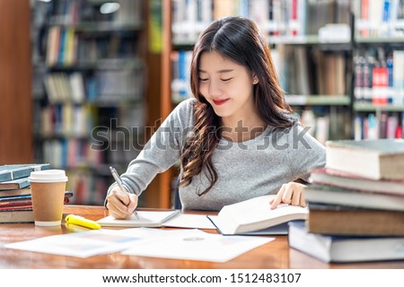 Asian young Student in casual suit reading and doing homework in library of university or colleage with various book and stationary on the wooden table over the book shelf background, Back to school Royalty-Free Stock Photo #1512483107