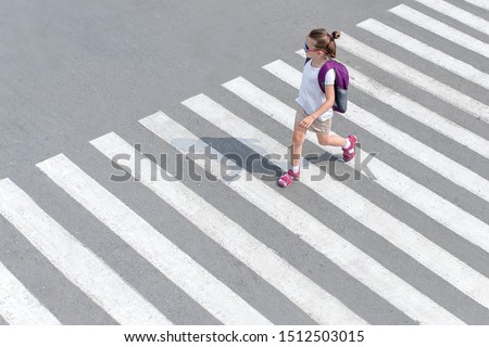 Schoolgirl crossing road on way to school. Zebra traffic walk way in the city. Concept pedestrians passing a crosswalk. Stylish young teen girl walking with backpack. 